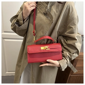 Detail view of red textured leather handbag with gold metal clasp and adjustable strap