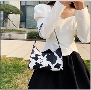 Close-up of cow print baguette bag featuring golden metal rings and leather texture