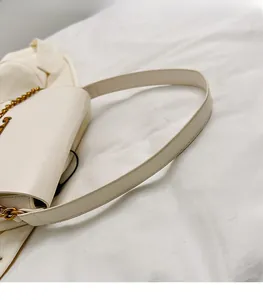 Detail of a beige shoulder bag with a smooth long strap and gold chain accessories