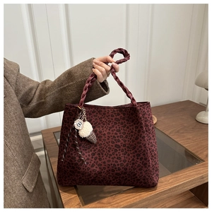 Close-up of a burgundy leopard print suede tote bag with woven handles and plush charm