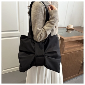 Detail view of large bow-knot design on black satin-finish tote bag in urban scene