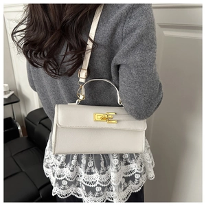Detail of a creamy white cross-grain leather handbag with golden twist lock and shoulder strap