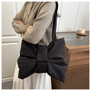 Dettaglio di una borsa a tracolla nera con grande fiocco indossata da una modella in interni