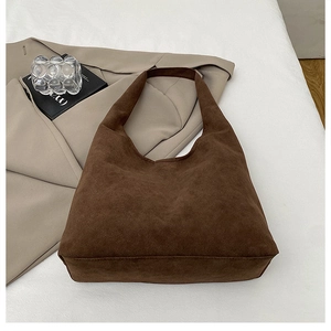 Detail of dark brown faux suede tote bag styled with blazer and books on clean background