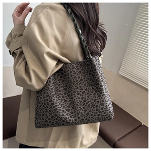 Detailed view of leopard print tote bag with woven green leather shoulder strap on model