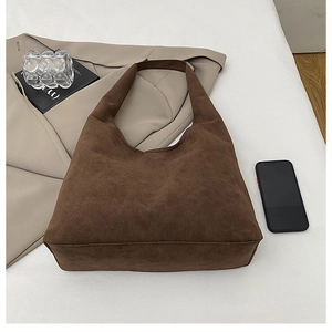 Flat lay of a large brown suede tote bag styled with a beige blazer and accessories