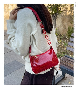 Red glossy embossed faux leather shoulder bag with chain strap shown in an outdoor setting
