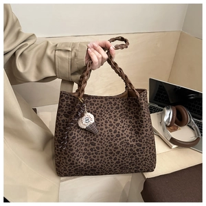 Detail of leopard print tote bag with brown woven handle and plush charm on a wooden desk