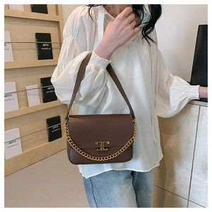 Detail of a dark brown leather crossbody bag with bold gold chain and T-shaped metal buckle