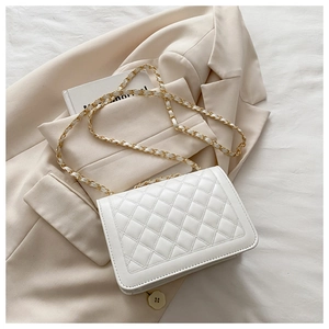 Close-up of quilted white leather shoulder bag with golden chain strap on beige blazer