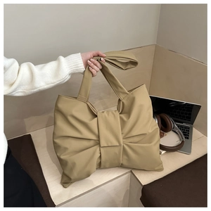 Grande borsa a tracolla kaki a forma di fiocco presentata in un ambiente lifestyle minimalista