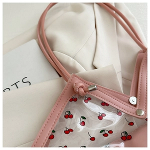 Dettaglio della borsa tote trasparente con stampa ciliegie, finiture rosa e rivetti in metallo