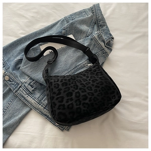 Detail of black leopard print crossbody bag with silver zipper on denim background