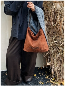 Detail view of brown suede hobo bag with white quilted stitching and metal chain strap