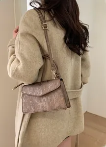 Detail of tan metallic textured crossbody bag with gold hardware on beige wool coat