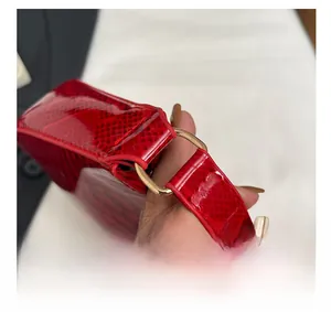 Close-up of golden metal D-ring hardware on a red snakeskin textured leather handbag