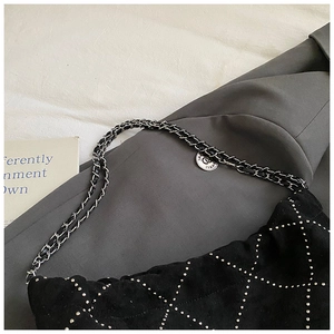 Close-up of black quilted suede bucket bag with gold rivets and chain strap detail