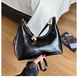 Détail du sac croissant noir en cuir verni avec une breloque sphérique dorée
