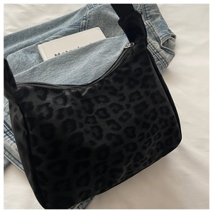 Leopard print underarm bag with glossy texture and zipper closure on white bedding