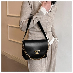 Detail of black leather crossbody bag with gold chain strap and metallic logo clasp