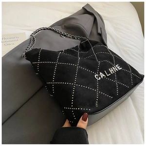 Detail of black suede tote bag featuring silver metal rivets and chain strap on a blazer