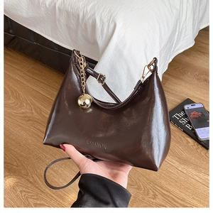 Détail d'un sac d'épaule marron foncé en cuir verni avec pendentif sphère dorée