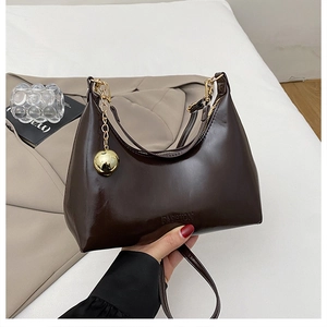 Détail du sac bandoulière en cuir marron avec breloque sphère dorée et logo gravé