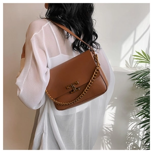 Brown leather crossbody bag with gold logo and chunky chain, worn by model on shoulder