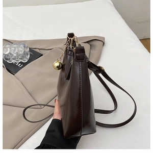 Détail du sac bandoulière brillant marron foncé avec charm boule dorée sur blazer