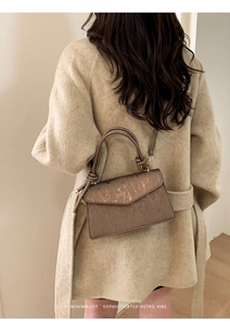 Detailed view of bronze textured small square bag with knotted handles worn with coat