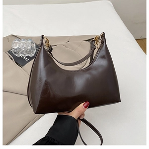 Detail van donkerbruine glanzende hobo-tas met gouden hardware en elegante ketting