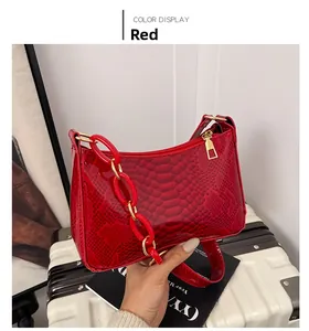 Detail of red snake-patterned underarm bag with decorative acrylic and metal chain link
