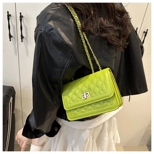 Detail of green quilted crossbody bag showing gold twist lock and chain strap on leather jacket