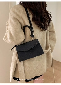 Detail of a black textured crossbody bag with unique knotted handle and metal rings