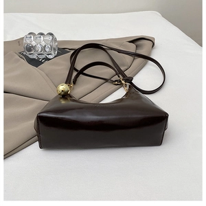 Détail d'un sac à main marron foncé brillant avec une boule dorée sur la bandoulière