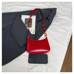 Detailed view of red snakeskin textured hobo bag with chain strap and phone for scale