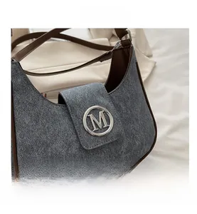 Close-up of retro gray denim underarm bag with brown leather trim and silver M logo