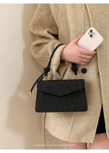 Close-up of minimalist black handbag with rope handle and textured finish on a beige coat