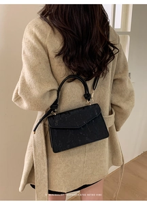Close-up of minimalist black rectangle flap bag with vertical texture and gold hardware