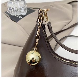 Détail d'un sac en cuir brillant marron foncé avec breloque sphérique dorée et chaîne chic