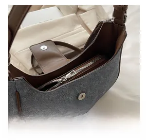 Detail of gray fabric crescent bag showing smooth metal zipper and leather trim closure