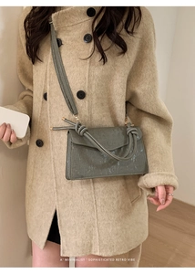 Detail of grey-green crossbody bag featuring textured fabric and unique knot shoulder strap