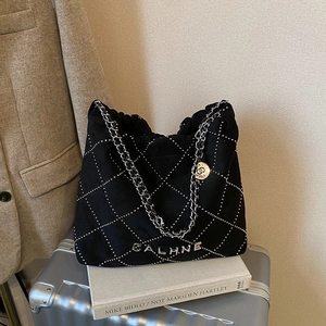 Quilted black knit tote bag with silver studs and chain handles on a silver suitcase