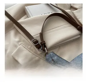 Detail of adjustable leather strap and metal buckle on grey saddle shoulder bag