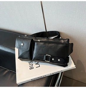 Detail of black pebbled leather crossbody bag with silver zippers on a white book