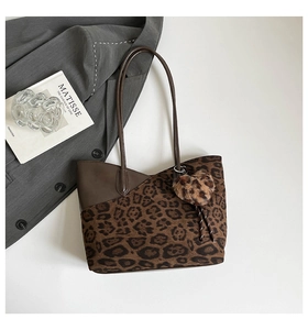 Detail of leopard print tote bag with plush heart charm on grey blazer backdrop