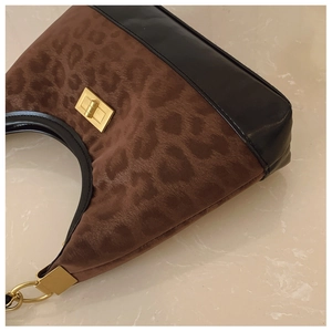 Detailed close-up of leopard print handbag featuring a gold twist lock and metal chain