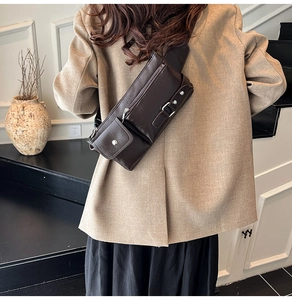 Detail of a dark brown leather crossbody bag with metal buckles and textured finish