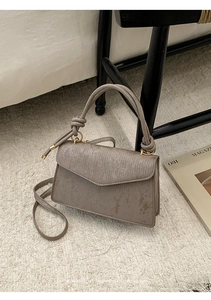 Detail of grey crossbody bag with vertical texture and golden hardware on plush carpet