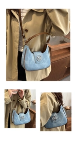 Detail of blue denim crescent bag with brown leather trim and silver metal M buckle